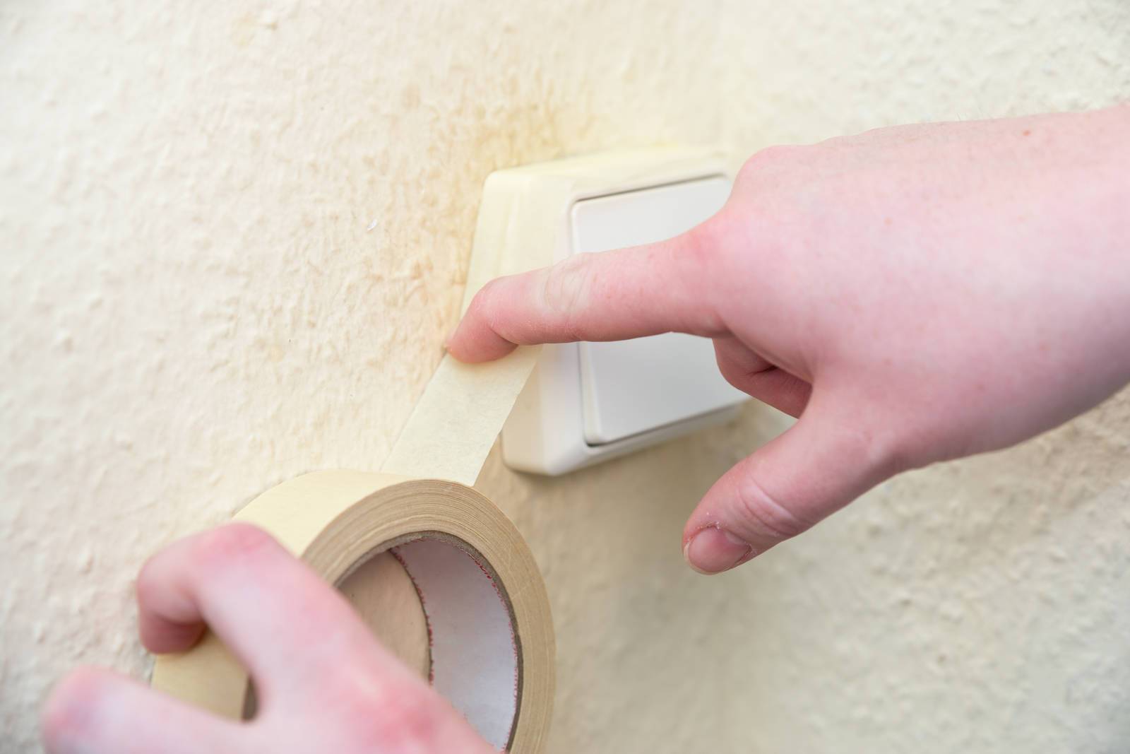 Malerband wird um einen Lichtschalter geklebt zur Untergrundvorbereitung beim Streichen